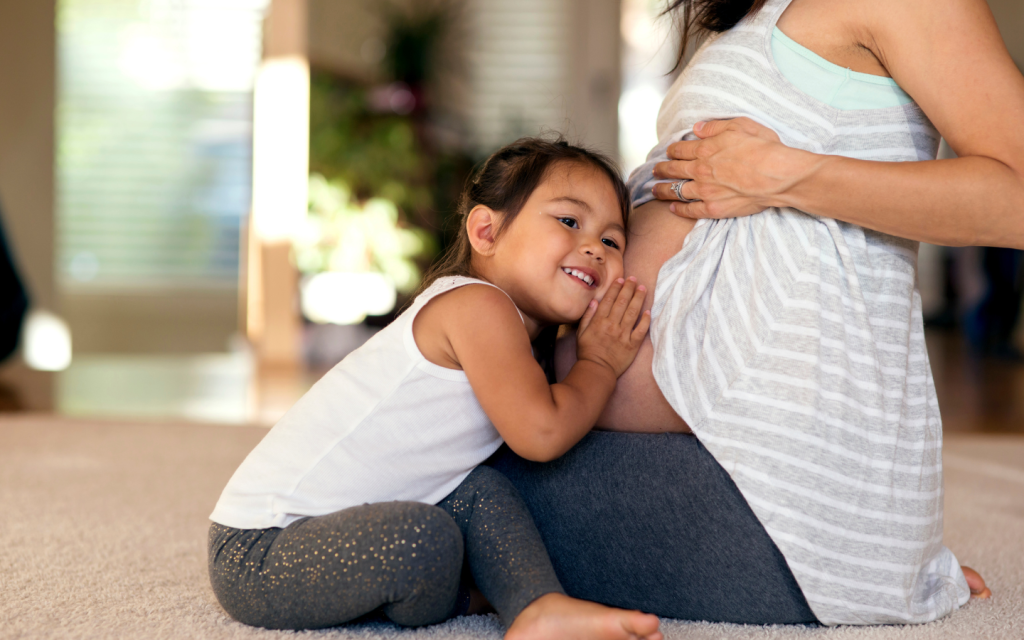 Pregnant person and child supporting one another with excitement.
